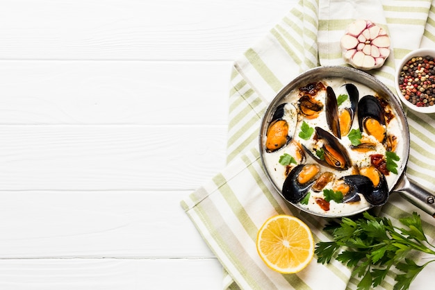 Flat-lay mussels in white sauce and sides on tablecloth with copyspace