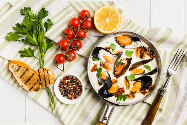 Flat-lay mussels in white sauce and sides on tablecloth