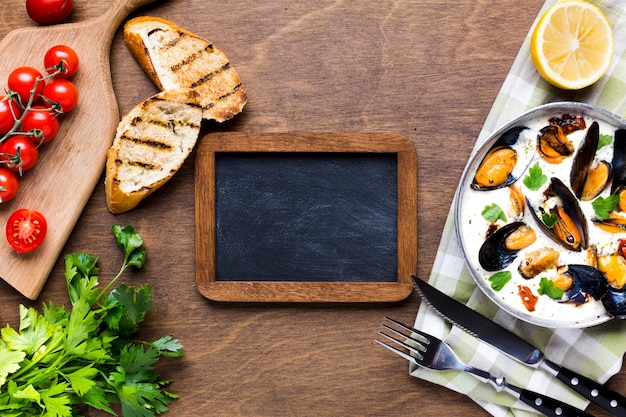 Flat-lay mussels in white sauce on tablecloth with blackboard