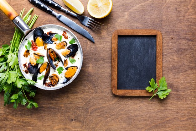 Flat-lay mussels in white sauce on tablecloth with blackboard