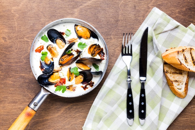 Flat-lay mussels in white sauce with tablecloth and cutlery