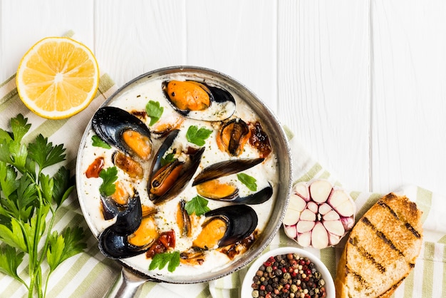 Flat-lay mussels in white and wine sauce on tablecloth with sides