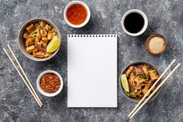 Flat lay noodles in bowls and sauces with blank notebook