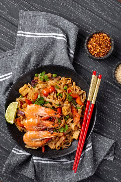 Flat lay noodles with vegetables and chicken with chopsticks and spices