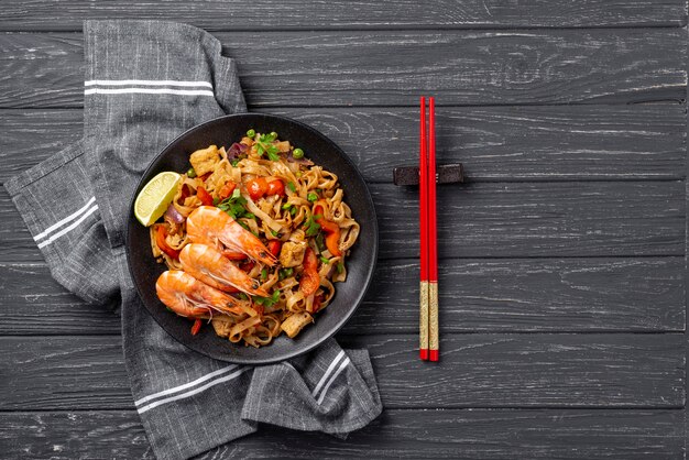 Flat lay noodles with vegetables and chicken with chopsticks