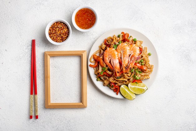 Flat lay noodles with vegetables and shrimp chopsticks and spices with wooden frame