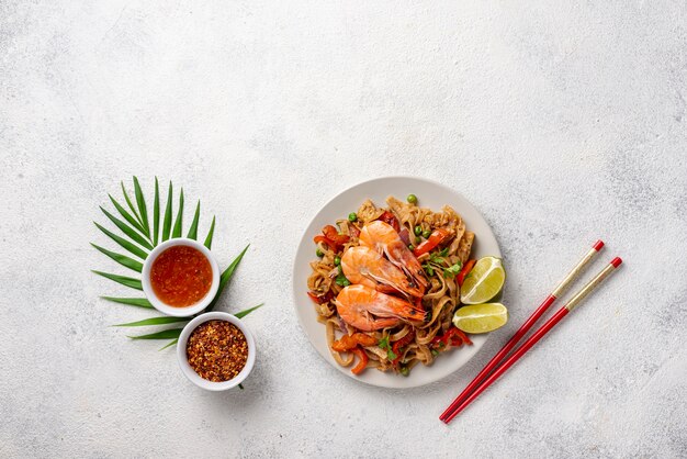 Flat lay noodles with vegetables and shrimp with chopsticks and spices