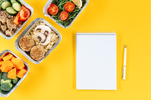 Flat lay of notebook with pen and meals in casseroles