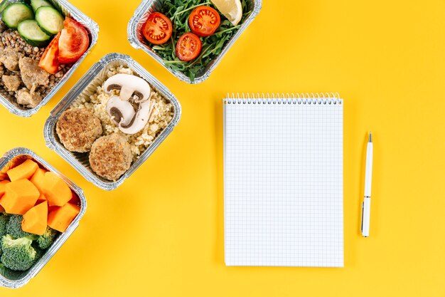 Flat lay of notebook with pen and meals in casseroles