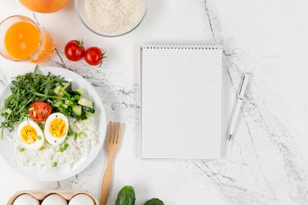 Flat lay of notebook with plate of rice and eggs