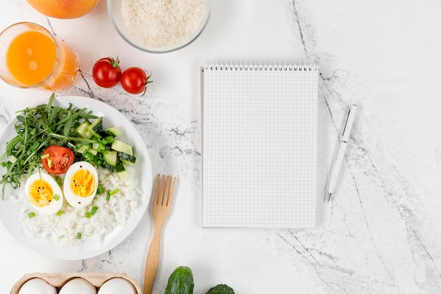 Flat lay of notebook with plate of rice and eggs