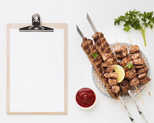 Flat lay of notepad with plate of delicious kebab and ketchup