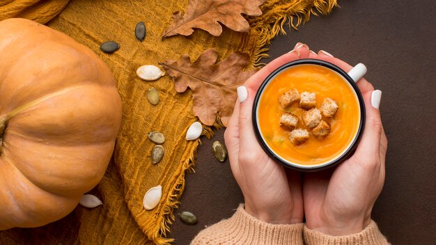 Бесплатное фото Плоская выкладка зимнего супа из кабачков с гренками в кружке в руках