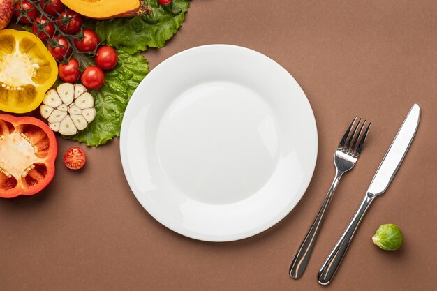 Плоская кладка органических овощей с тарелкой и столовыми приборами
