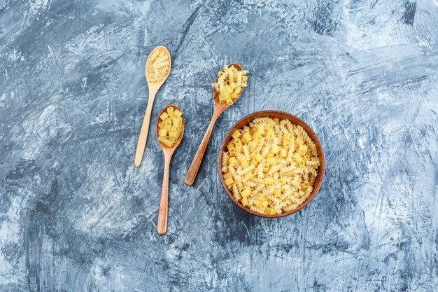 Flat lay pasta in clay bowl and wooden spoons on grungy plaster background. horizontal