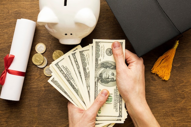 Flat lay of piggy bank with academic cap and banknotes