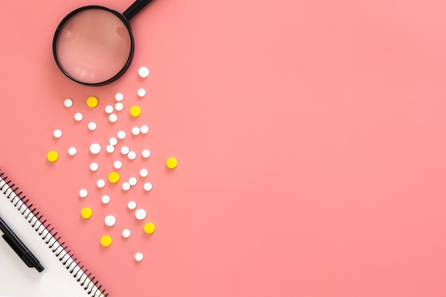 Flat lay pills and magnifier on pink background copy space