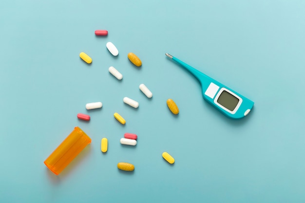 Flat lay of pills with thermometer and plastic container