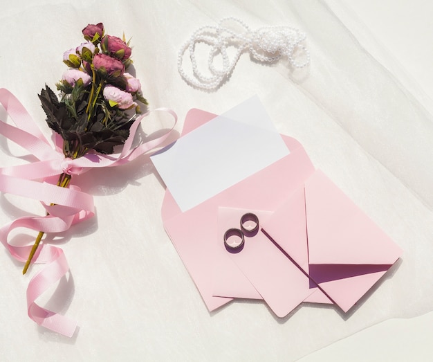 Flat lay pink wedding invitation next to bouquet of roses