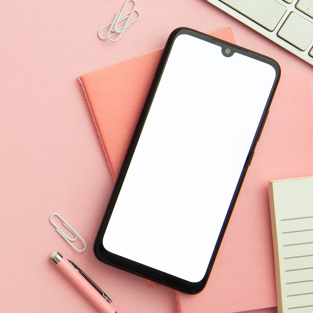 Flat lay pink workplace arrangement with empty phone close-up