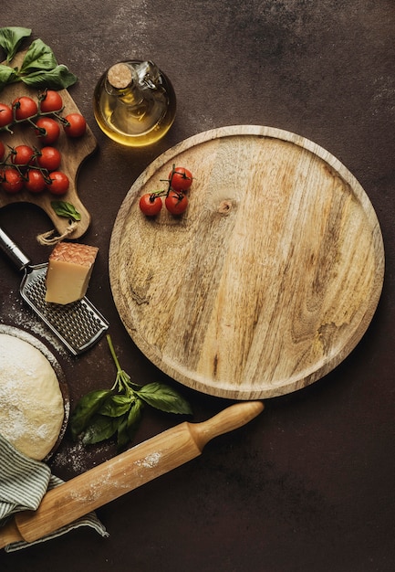 Flat lay of pizza dough with wooden board and tomatoes