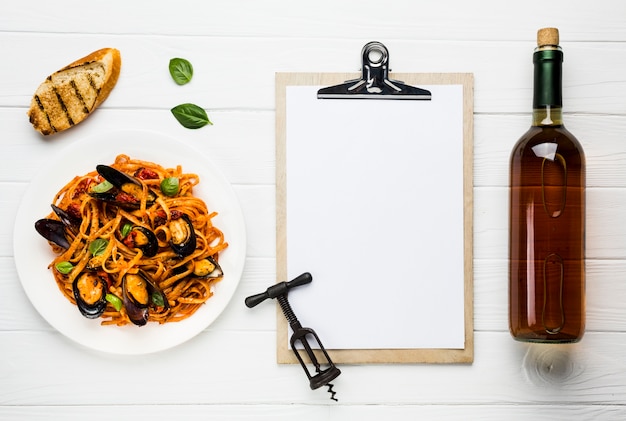 Flat-lay plate of mussels pasta and wine with clipboard