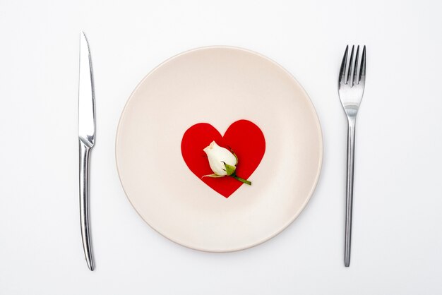 Flat lay of plate with heart and cutlery with rose