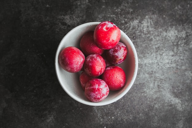 Flat lay plums in bowl on black textured.