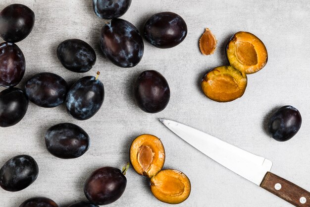 Flat lay of plums and knife on wooden background