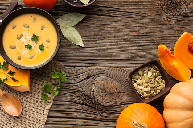 Flat lay pumpkin soup in bowl with pumpkin and wooden spoon and seeds