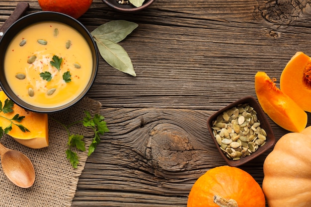 Flat lay pumpkin soup in bowl with pumpkin and wooden spoon and seeds