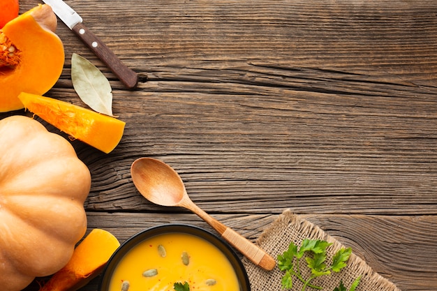 Flat lay pumpkin soup in bowl with pumpkin and wooden spoon with copy space