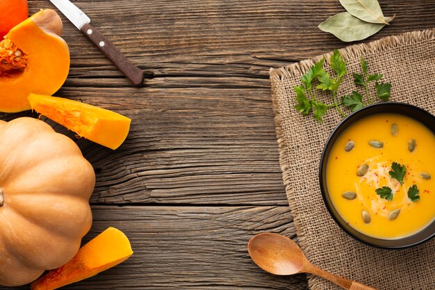 Flat lay pumpkin soup in bowl with pumpkin and wooden spoon