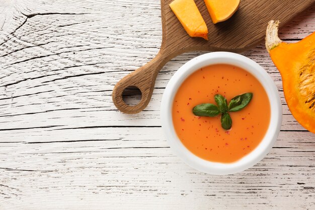 Flat lay pumpkin soup and pumpkin on cutting board with copy space