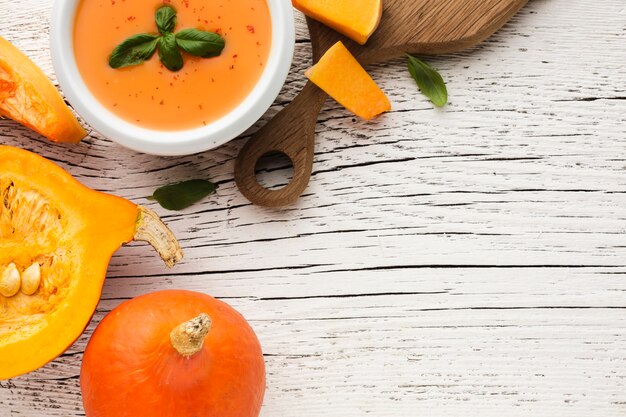 Flat lay pumpkin soup and pumpkin on wooden cutting board with copy space