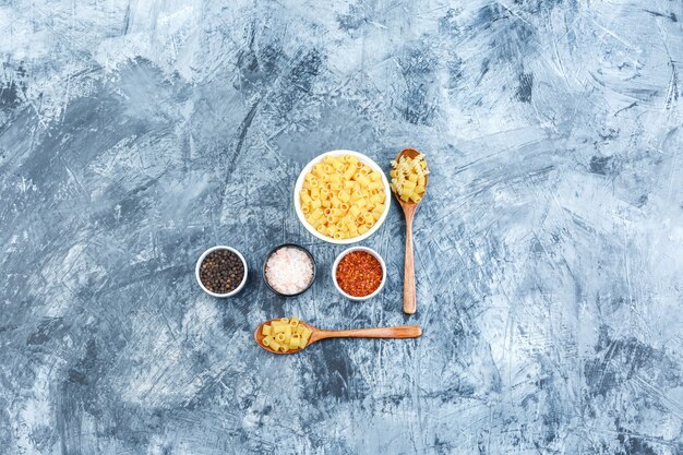 Flat lay raw pasta in bowl and wooden spoons with spices on grungy plaster background. horizontal