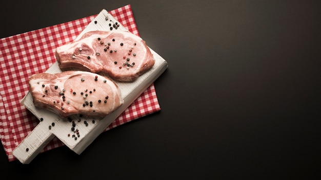 Flat lay raw steaks on wooden board with pepper with copy-space