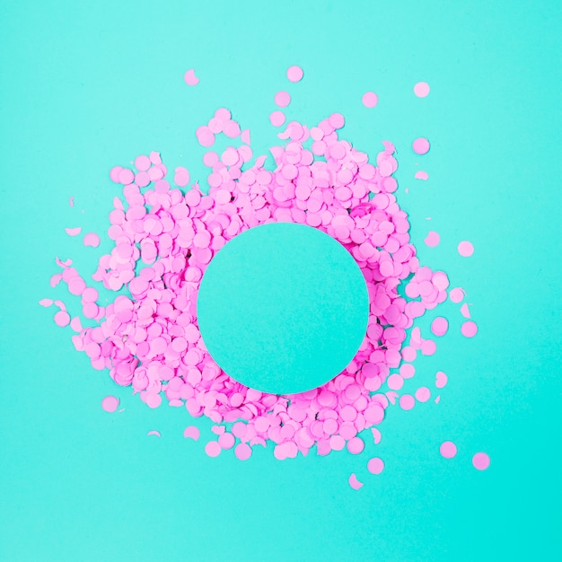 Flat lay of round paper pink confetti on turquoise paper with clear circle in middle