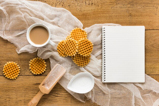 Flat lay of round waffles on wooden surface with notebook and coffee