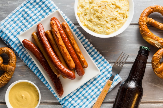 Flat lay of sausages with pretzels with beer bottle