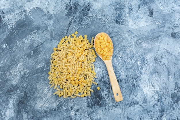 Flat lay scattered pasta in wooden spoon on grungy plaster background. horizontal