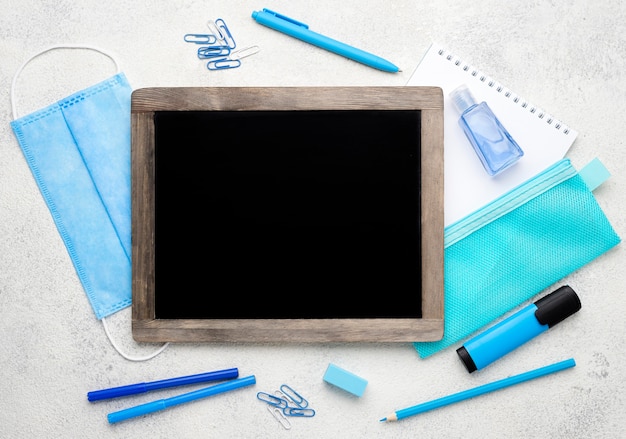 Flat lay of school essentials with blackboard and medical mask