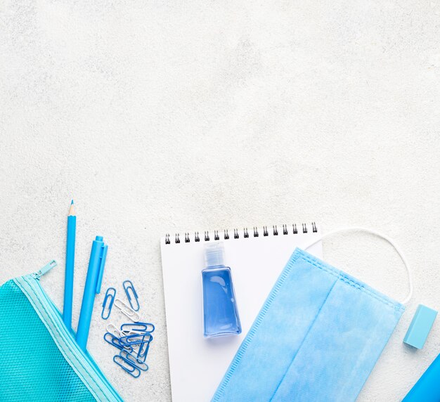 Flat lay of school essentials with paper clips and medical mask