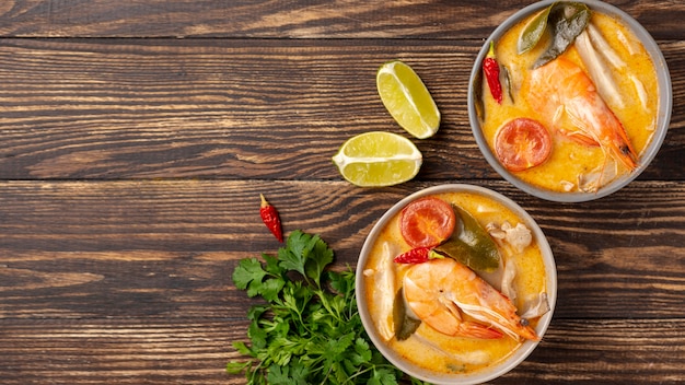 Flat lay soups in bowls with shrimp on wooden background with copy space