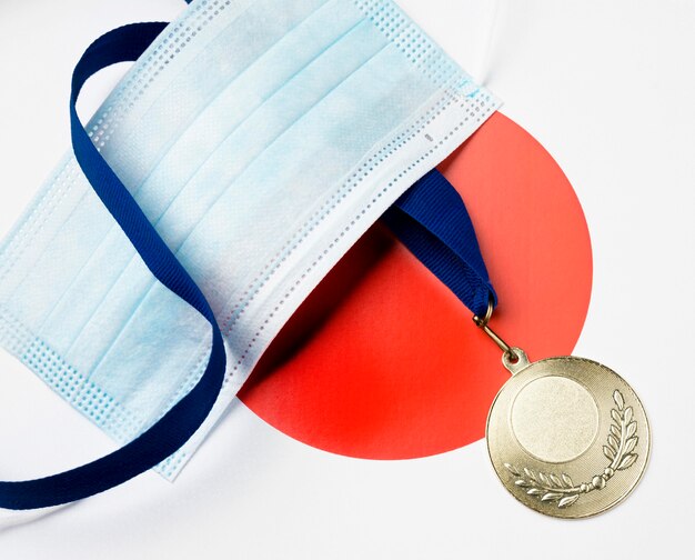 Плоская спортивная медаль рядом с медицинской маской
