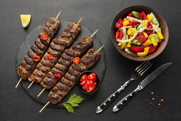 Flat lay of tasty kebab on slate with other dish and cutlery