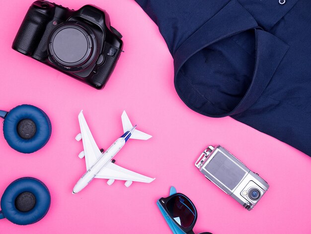 Плоский вид сверху аксессуаров фотографа путешественника на розовом фоне. фотоаппарат, солнцезащитные очки. наушники. Рубашка