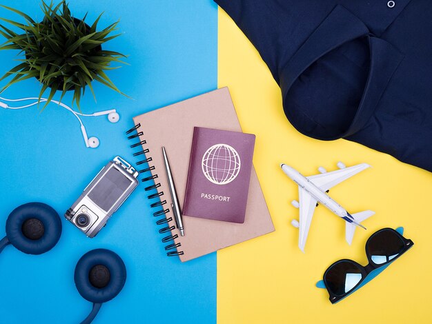 黄色の背景に旅行者の写真家のアクセサリーのフラットレイトップビュー。カメラ、サングラス、パスポート。ノートブック。シャツ