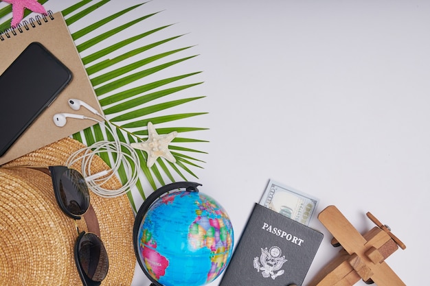 Flat lay travel accessories on white background with palm leaf, camera, hat, passports, money, globe, book, phone, map, and sunglasses. Top view, travel or vacation concept. Summer background.