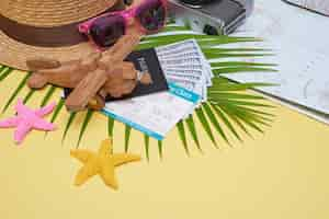 Free photo flat lay traveler accessories on yellow surface with palm leaf, camera, shoe, hat, passports, money, air tickets, airplanes and sunglasses. top view, travel or vacation concept.